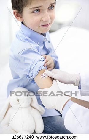 Stock Image - Doctor putting plaster on boy's arm after injection. Fotosearch