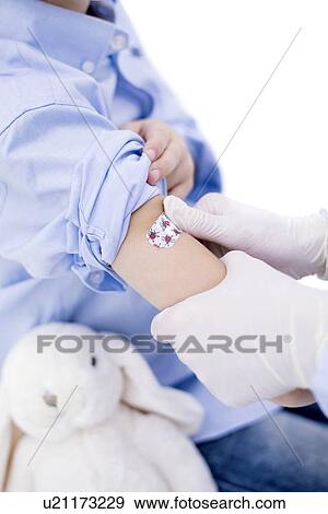 Stock Photo - Doctor putting plaster on boy's arm after injection. Fotosearch