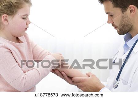 Stock Image - Male doctor examining girl's arm.. Fotosearch