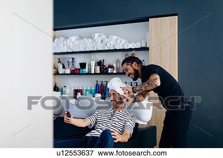 Stock Photo - Male hairstylist and male customer taking smartphone selfie in hair salon. Fotosearch