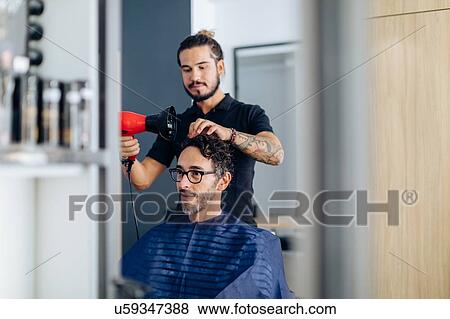 Stock Photo - Male hairstylist blow drying male customer's hair in hair salon. Fotosearch