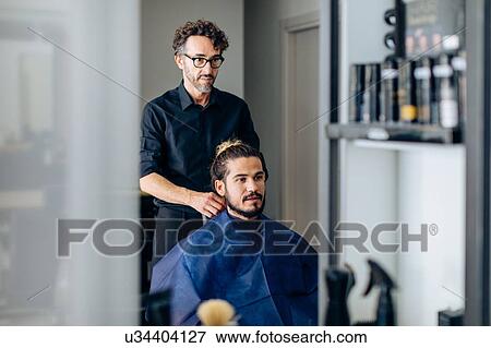 Male hairstylist putting on male customer's cape at hair salon View Large Photo Image Stock Photo - Male hairstylist putting on male customer's cape at hair salon. Fotosearch