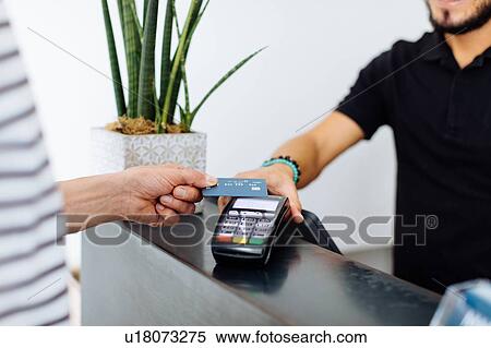 Stock Photography - Male hairstylist taking male customer's credit card payment at hair salon, cropped. Fotosearch
