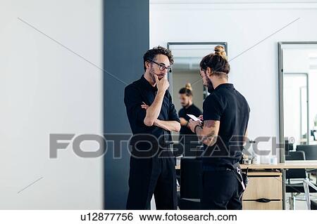 Male hairstylists chatting and looking at smartphone in hair salon View Large Photo Image Stock Photograph - Male hairstylists chatting and looking at smartphone in hair salon. Fotosearch