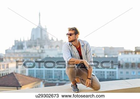 Stock Image - Man on edge of rooftop terrace, Milan, Italy. Fotosearch
