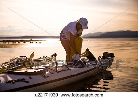 Stock Photo - Mature female kayaker preparing kayak at sunset, Quadra Island, Campbell River, Canada. Fotosearch