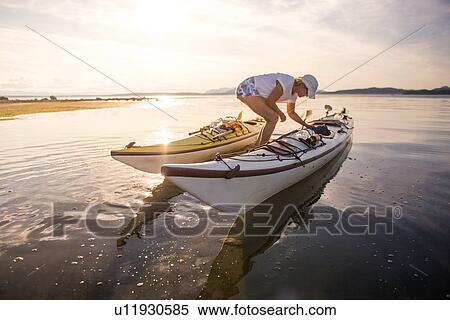 Stock Photography - Mature female kayaker preparing kayaks, Quadra Island, Campbell River, Canada. Fotosearch
