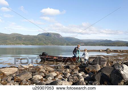 Stock Image - Mature man passing rope to son from rowing boat, Aure, More og Romsdal, Norway. Fotosearch
