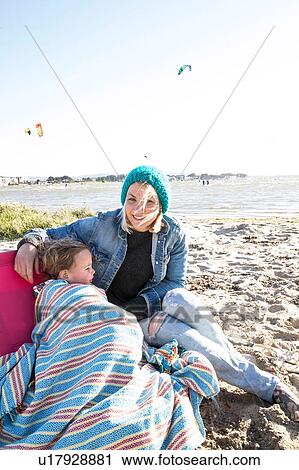 Stock Image - Mother and toddler girl in blanket on beach. Fotosearch