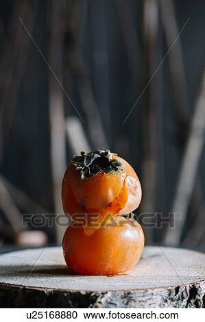 Stock Image - Persimmon fruit on top of another on rustic cutting board. Fotosearch