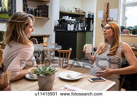 Stock Image - Pregnant mid adult woman and best friend chatting over coffee in cafe. Fotosearch