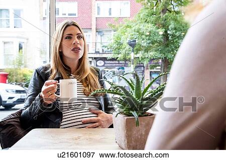 Stock Photo - Pregnant mid adult woman chatting with friend in cafe. Fotosearch