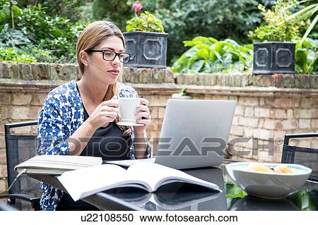 Stock Image - Pregnant mid adult woman looking at laptop on patio table. Fotosearch