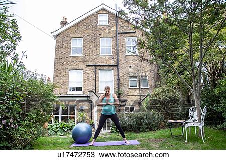 Stock Image - Pregnant mid adult woman practicing yoga in garden. Fotosearch