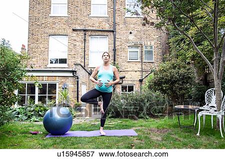 Stock Photo - Pregnant mid adult woman practicing yoga tree pose in garden. Fotosearch