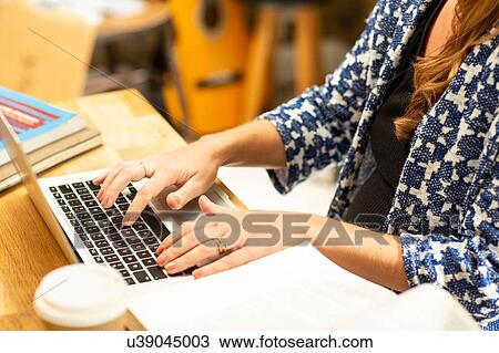 Stock Image - Pregnant mid adult woman typing on laptop at kitchen table, cropped. Fotosearch