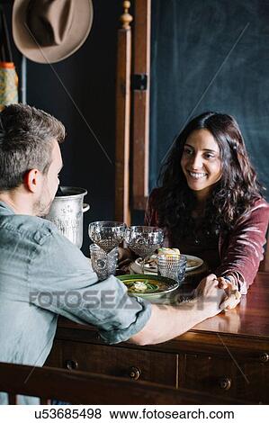 Stock Photo - Romantic young couple having a meal, holding hands across table. Fotosearch