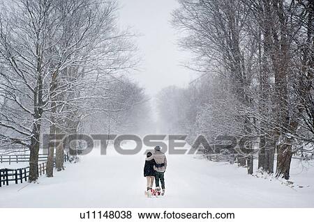 Stock Photo - Romantic young couple walking dog in snow covered forest, rear view, Ontario, Canada. Fotosearch
