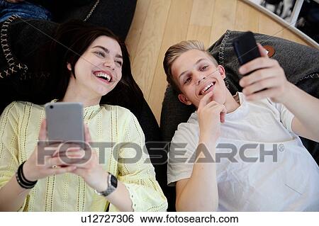 Stock Photograph - School friends lying on beanbags and texting at school. Fotosearch