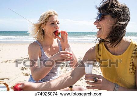 Picture - Sisters enjoying picnic on beach. Fotosearch