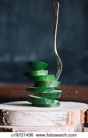 Stock Photograph - Stacked sliced courgettes and fork on rustic cutting board. Fotosearch