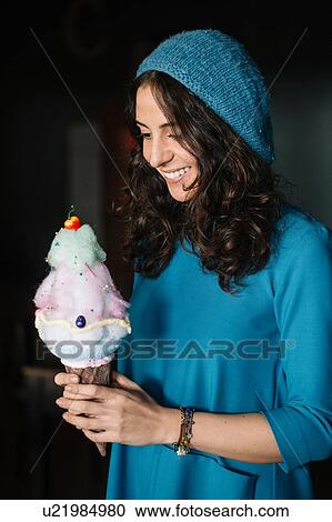 Stock Image - Stylish young woman in blue knit hat holding large ice cream cone. Fotosearch