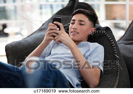 Teenage boy lying on beanbag and reading text message on cellphone View Large Photo Image Stock Photo - Teenage boy lying on beanbag and reading text message on cellphone. Fotosearch