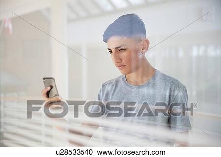 Teenage boy reading text message on cellphone by glass wall View Large Photo Image Stock Image - Teenage boy reading text message on cellphone by glass wall. Fotosearch
