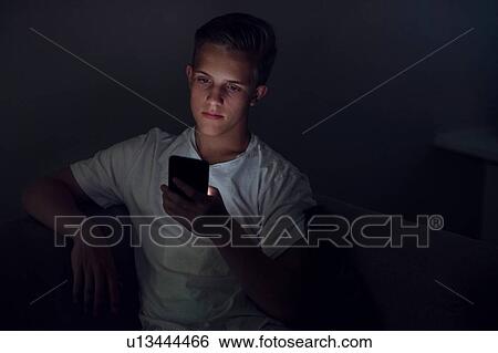 Teenage boy sitting on sofa in dark reading text message View Large Photo Image Stock Photograph - Teenage boy sitting on sofa in dark reading text message. Fotosearch