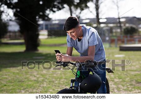 Stock Image - Teenage boy texting on pushbike. Fotosearch