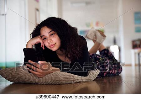 Stock Photo - Teenage girl lying on cushion on floor reading text message. Fotosearch
