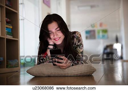 Stock Photograph - Teenage girl lying on cushion on floor reading text message. Fotosearch