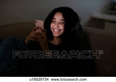 Teenage girl lying on sofa in dark reading text message View Large Photo Image Picture - Teenage girl lying on sofa in dark reading text message. Fotosearch