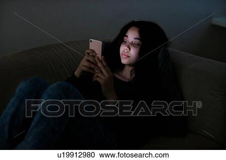 Teenage girl lying on sofa in dark reading text message View Large Photo Image Stock Image - Teenage girl lying on sofa in dark reading text message. Fotosearch
