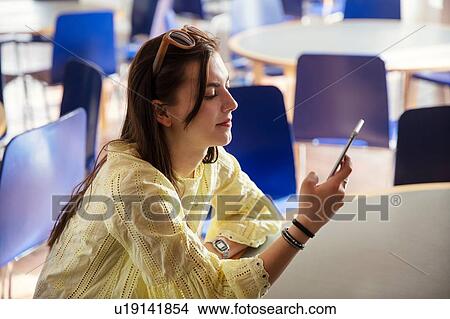 Picture - Teenage girl reading text message on cellphone in school. Fotosearch