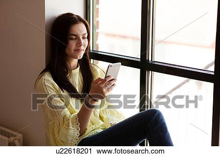 Teenage girl reading text message on cellphone by glass window View Large Photo Image Stock Image - Teenage girl reading text message on cellphone by glass window. Fotosearch