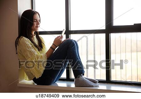 Stock Photo - Teenage girl reading text message on cellphone by glass window. Fotosearch