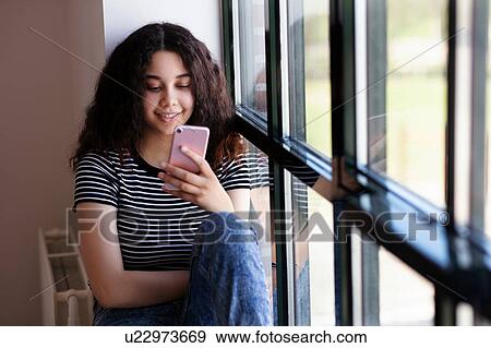 Teenage girl reading text message on cellphone by glass window View Large Photo Image Stock Photo - Teenage girl reading text message on cellphone by glass window. Fotosearch