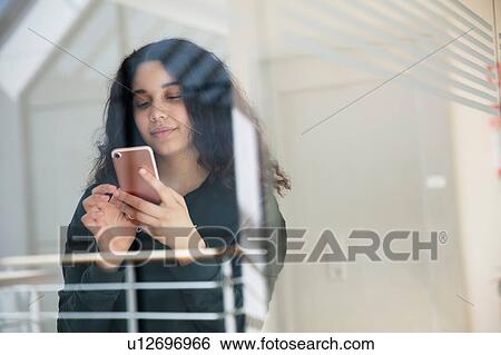 Teenage girl reading text message on cellphone by glass wall View Large Photo Image Stock Photograph - Teenage girl reading text message on cellphone by glass wall. Fotosearch