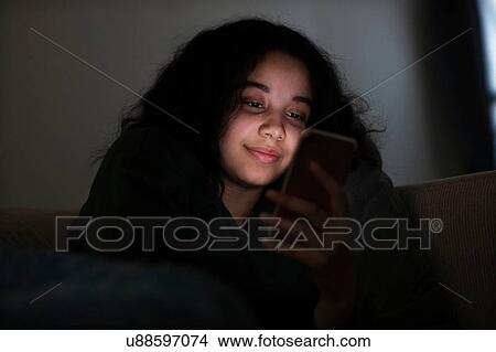 Teenage girl sitting on sofa in dark reading text message View Large Photo Image Picture - Teenage girl sitting on sofa in dark reading text message. Fotosearch