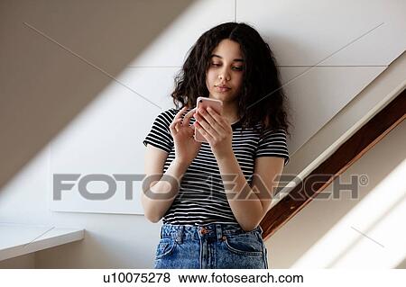 Stock Photo - Teenage girl texting in room. Fotosearch