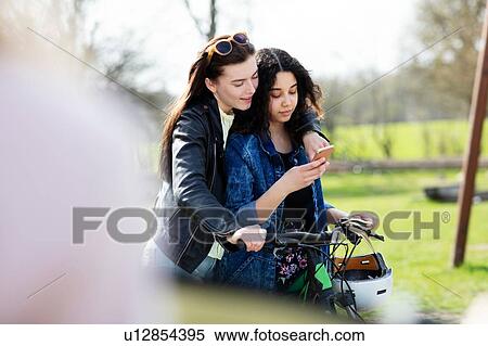 Teenage girls reading text together on push bike View Large Photo Image Stock Photography - Teenage girls reading text together on push bike. Fotosearch