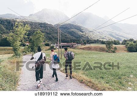 Stock Image - Three young adult friends hiking along dirt track, rear view, Primaluna, Trentino-Alto Adige, Italy. Fotosearch