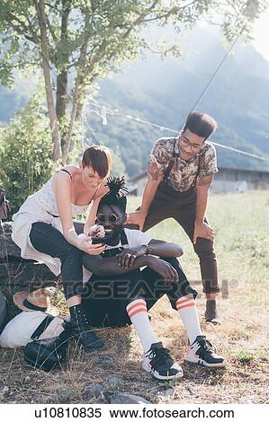 Stock Photography - Three young adult hikers in field looking at smartphone, Primaluna, Trentino-Alto Adige, Italy. Fotosearch