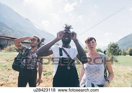 Stock Photo - Three young hiking friends looking up through binoculars from field landscape, Primaluna, Trentino-Alto Adige, Italy. Fotosearch