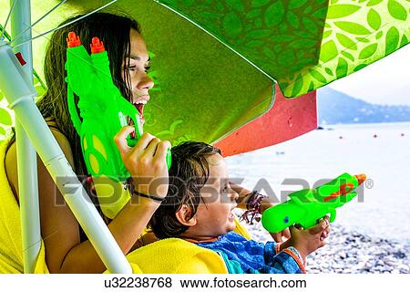 Woman and boy playing with water pistols on beach View Large Photo Image Stock Photo - Woman and boy playing with water pistols on beach. Fotosearch