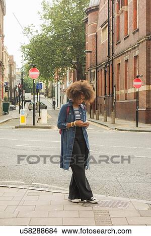 Picture - Woman checking cellphone on pavement, London, UK. Fotosearch