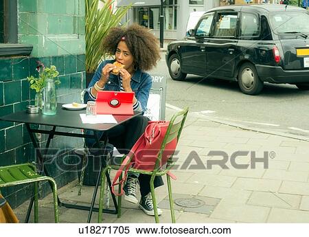 Stock Photography - Woman eating and using digital tablet at pavement cafe, London, UK. Fotosearch