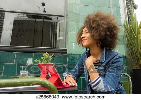 Woman looking up from digital tablet at pavement cafe, London, UK View Large Photo Image Stock Photo - Woman looking up from digital tablet at pavement cafe, London, UK. Fotosearch