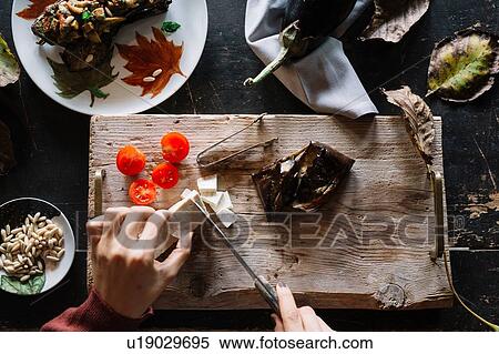 Stock Photography - Woman slicing cheese on rustic chopping board, overhead view of hands. Fotosearch